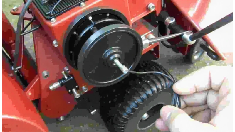 A detailed view of a snow blower's recoil starter assembly with the cover removed, showing the pull cord pulley and spring.