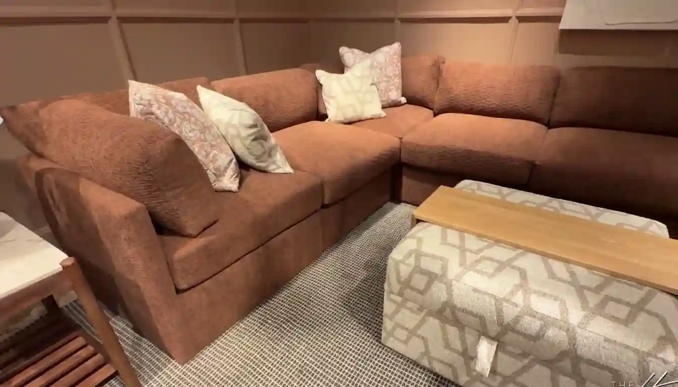 A close-up of the detailed stitching on a Maroon fabric sofa with a wooden leg on a light-colored rug.