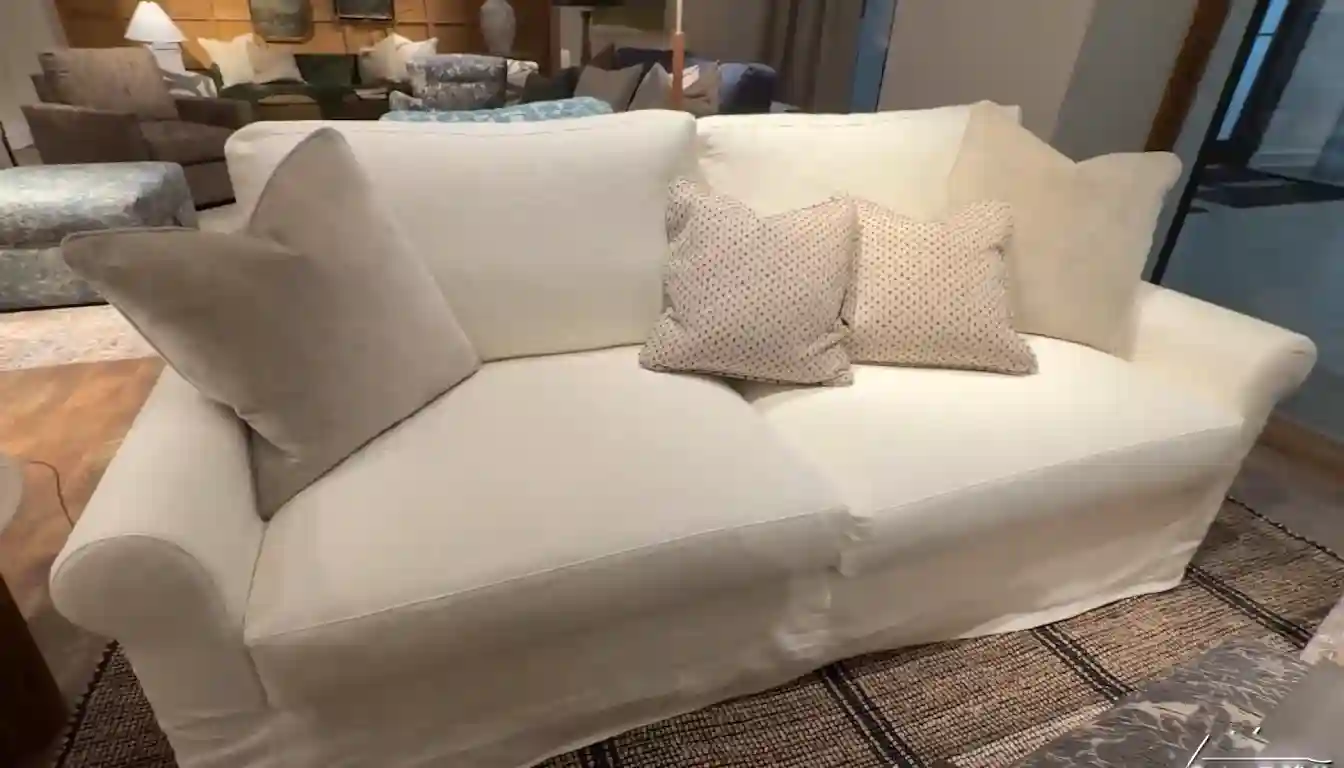 A close-up of the detailed stitching on a white fabric sofa with a wooden leg on a light-colored rug.