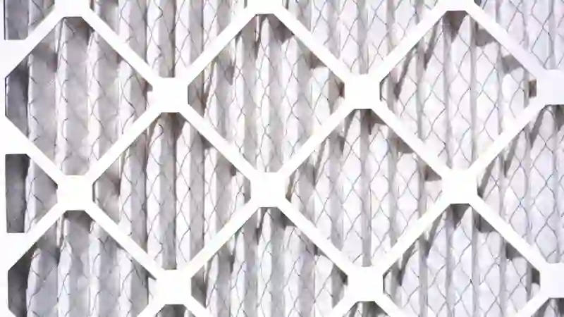 A close-up of a clean, white, pleated HVAC air filter, showing the fibrous texture of the filter media and the cardboard frame.