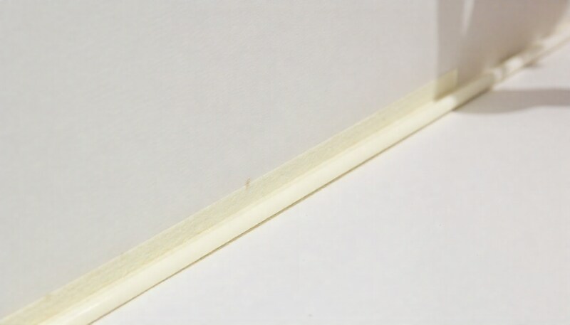 A gray foam backer rod being inserted into a large gap between a white bathtub surround and a beige tiled wall before the application of white sealant.