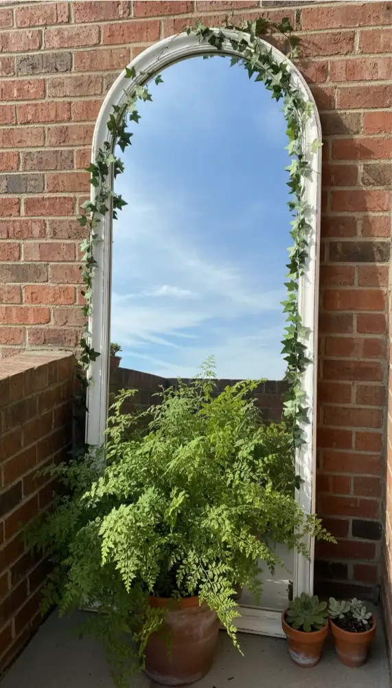 Decorative mirror hanging on a balcony wall reflecting greenery