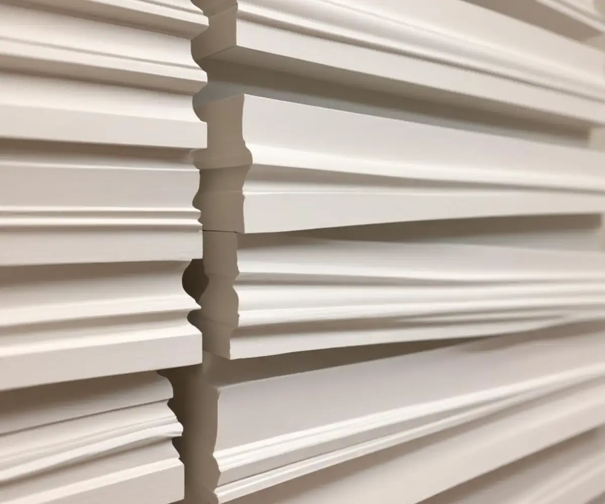 A stack of various white primed baseboard moulding profiles.