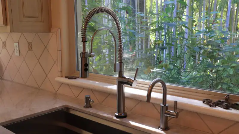 A sleek, matte black Brizo Odin pull-down kitchen faucet installed on a white quartz countertop next to a stainless steel sink.