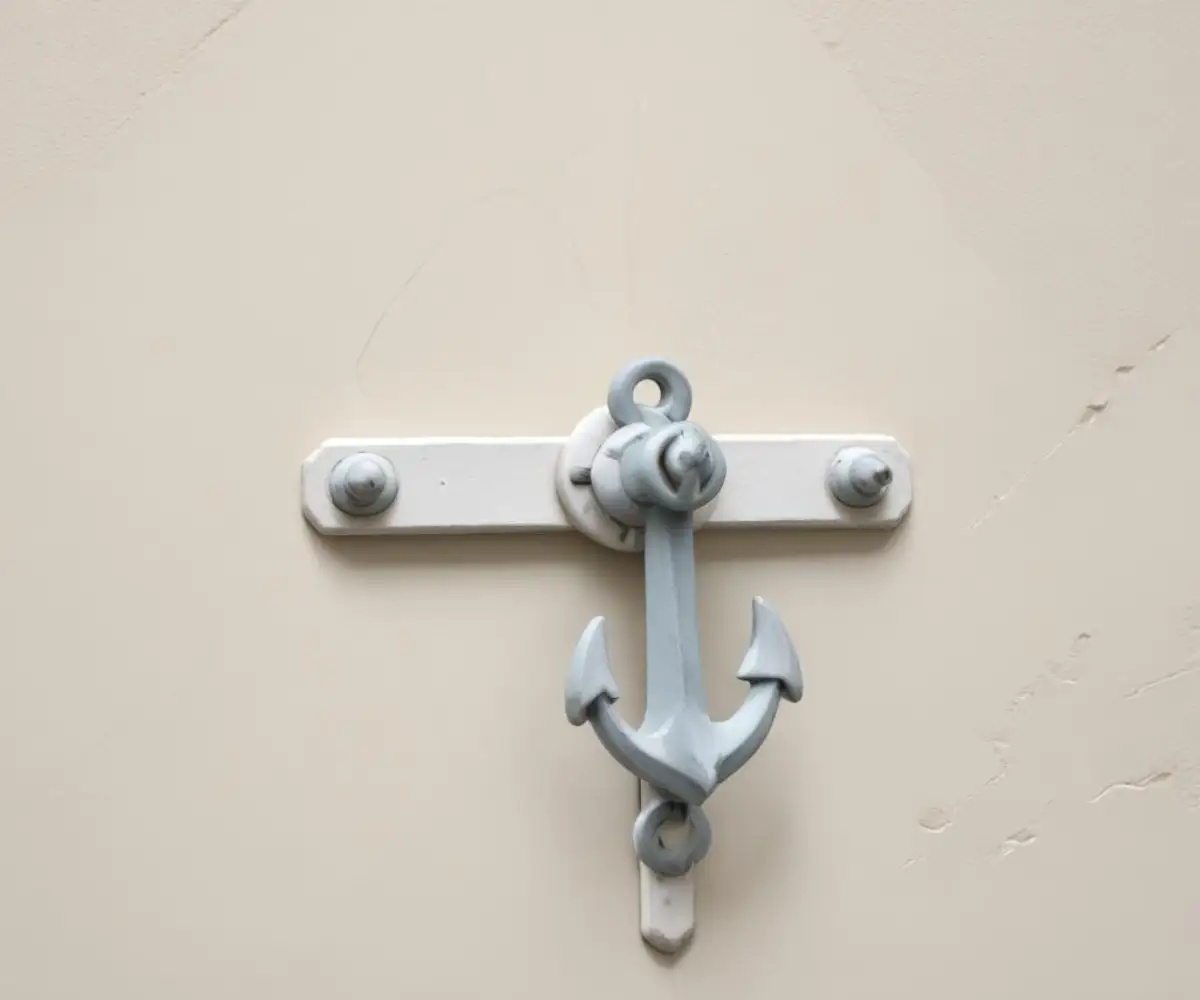 A close-up view of a metal toggle bolt anchor set securely into a smooth, white plaster wall.