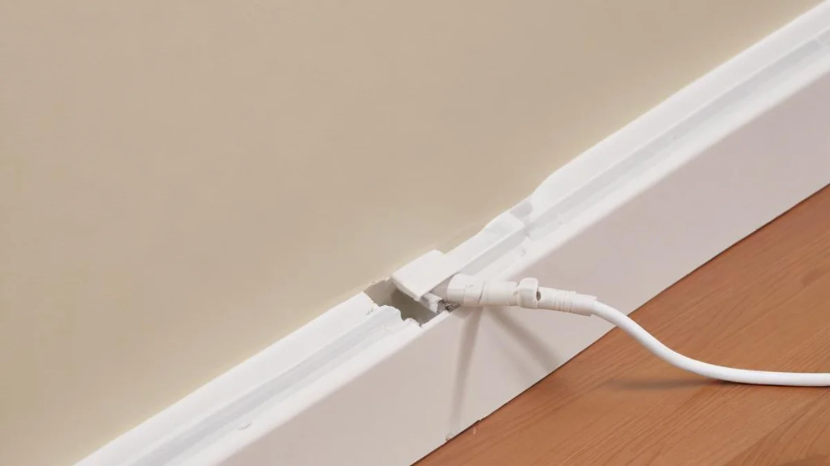 White plastic wire molding concealing exposed Romex cable along the base of a wall.