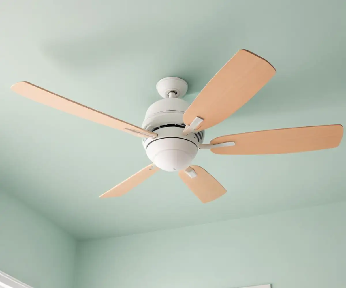 A modern ceiling fan with wooden blades and a central light fixture, mounted on a plain white ceiling.