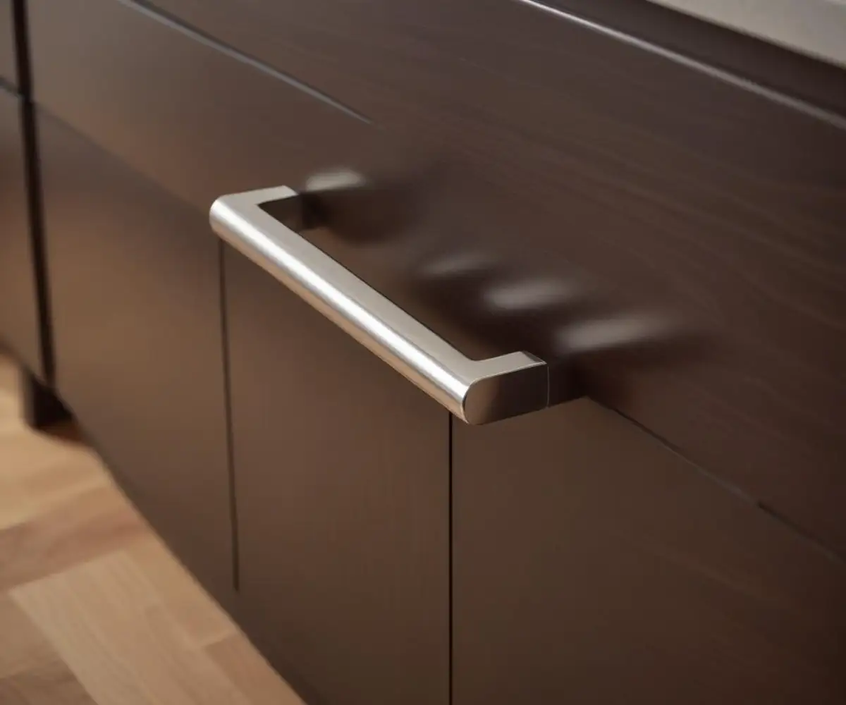 A close-up of a polished nickel cabinet pull with a classic bar design, mounted horizontally on a dark wood kitchen drawer.