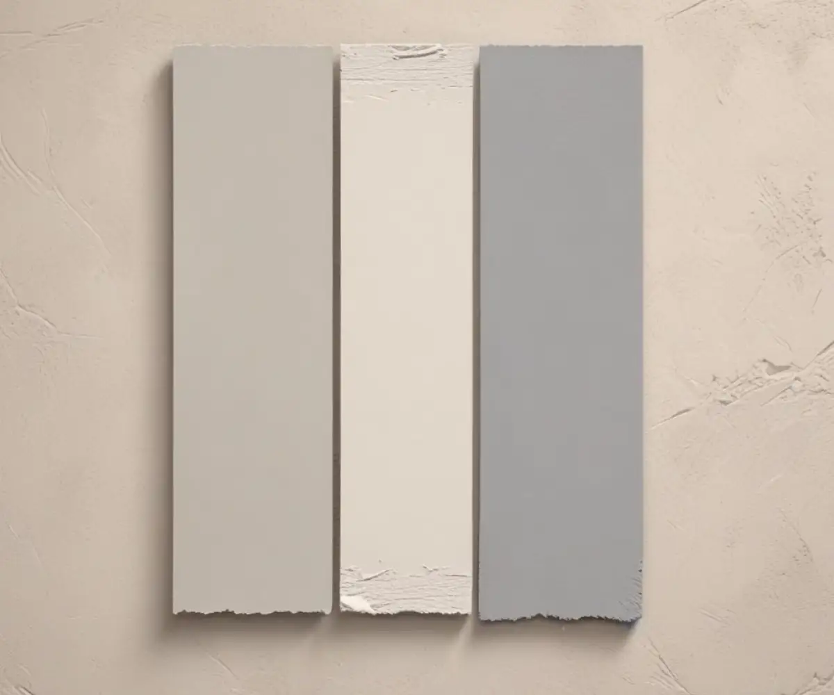 A side-by-side comparison of two greige paint swatches, Revere Pewter and Worldly Gray, on a textured wall.