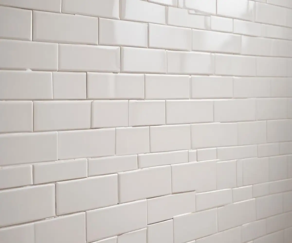 A close-up of a freshly installed white subway tile wall showing very tight, consistent grout lines in a running bond pattern.