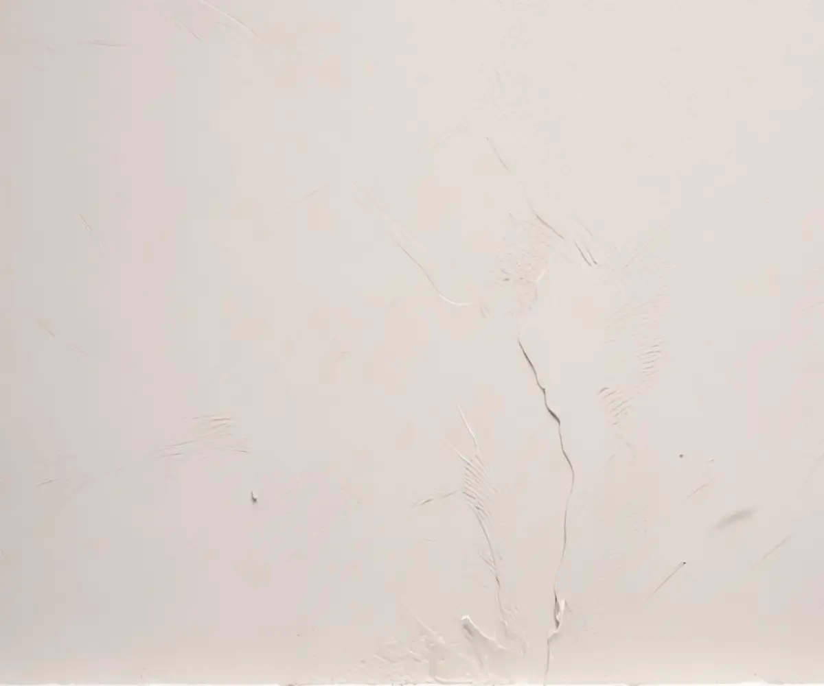 A close-up view of a wall with a thick, textured white paint application, showing distinct brush or roller marks.