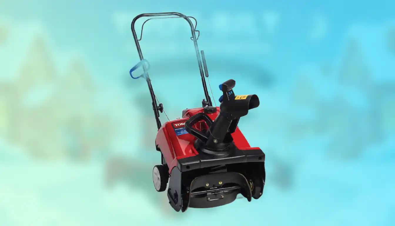 A red single-stage snow blower resting on a clean concrete driveway next to a closed garage door.