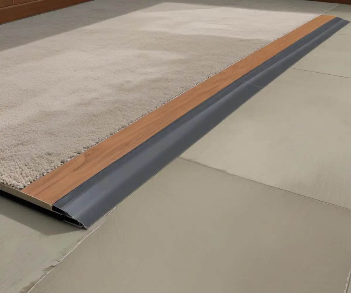 A metal transition strip joining luxury vinyl plank flooring to plush carpet on a concrete slab.