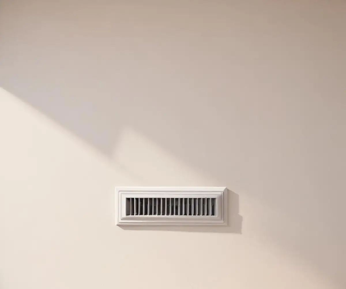 Close-up of a pristine, white air vent on a light-colored interior wall.